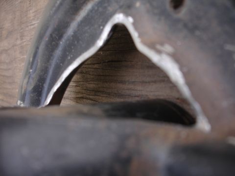 1995 Ford Taurus - A close-up view of a black metal suspension component, possibly a knuckle brace, against a wooden background.