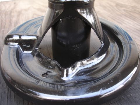 1995 Ford Taurus - Black metal suspension part with a circular base and central shaft, resting on a wooden surface.