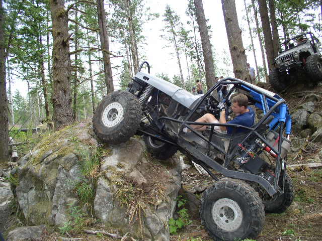 Off-road vehicle with roll cage climbing a large rock, driver visible