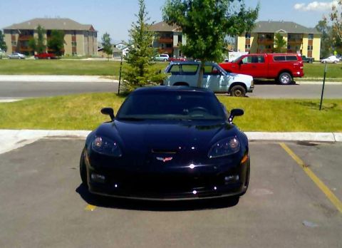 2006 Ford E350 - Front view of a black Chevrolet Corvette C6 parked in a lot with other vehicles behind it.