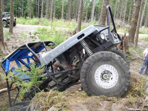 1979 Ford Bronco - An off-road buggy with a custom roll cage and large tires is tilted on a rocky incline in a wooded area.