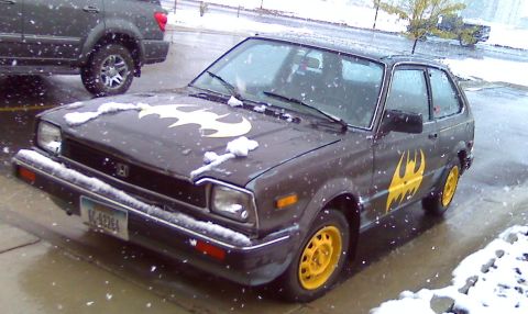 2006 Ford E350 - A dark gray Honda Civic hatchback, adorned with Batman decals and yellow wheels, sits in the snow.