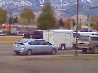 2006 Ford E350 - A light blue Toyota Prius is seen driving in a parking lot next to a white cargo trailer and a van.