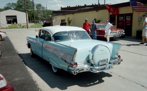 2006 Ford E350 - A classic 1957 Chevrolet Bel Air is parked next to a red 1960s sedan, with people standing nearby.