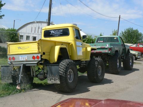 2006 Ford E350 - Modified pickup trucks with oversized tires are parked in a lot. The yellow truck has custom graphics.
