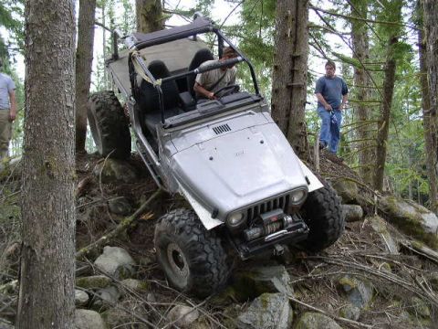 1979 Ford Bronco - Jeep Wrangler tackling a challenging off-road course in a forest setting.