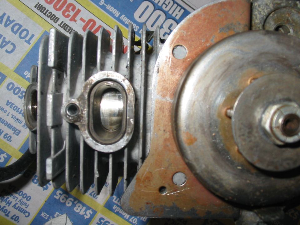 Close-up of a small air-cooled engine's finned cylinder and rusty flywheel cover on newspaper