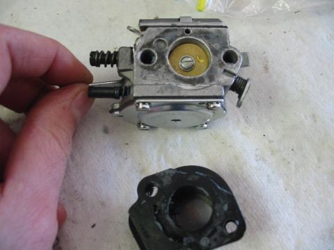 1992 Ford Bronco - A hand holds a carburetor part, with a gasket lying nearby on a white surface.