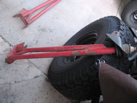 1986 Ford Bronco - Red radius arms, likely for an off-road vehicle, are shown next to a large tire.
