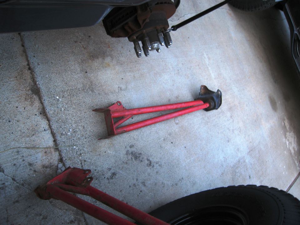 Two red suspension control arms and a vehicle's brake rotor and hub assembly on a concrete surface
