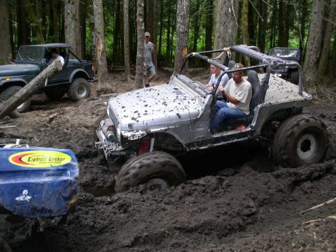 1979 Ford Bronco - Two Jeeps navigate a muddy forest trail, one deeply stuck.