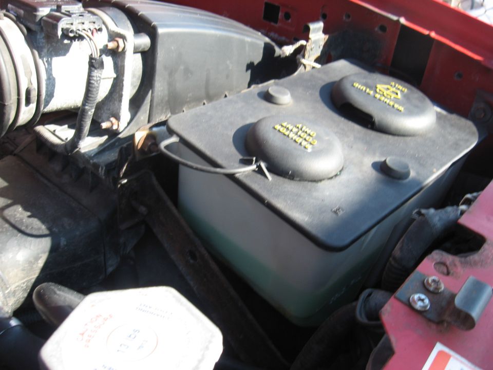 Black brake fluid master cylinder reservoir with twin caps in an engine bay, red fender at right.