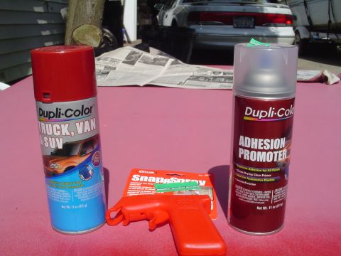 1996 Ford Bronco - Spray paint cans and a spray trigger are laid out on a pink surface, with a silver sedan visible in the background.