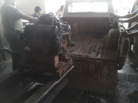 1986 Ford Bronco - An engine is being loaded into the bed of an older pickup truck.