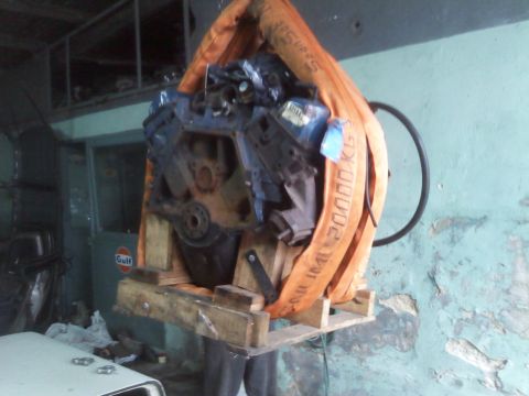 1986 Ford Bronco - An engine is being lifted by orange straps and a wooden pallet in a workshop.