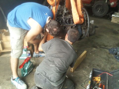 1986 Ford Bronco - Two mechanics are working on an engine that is suspended by an engine hoist in a garage.
