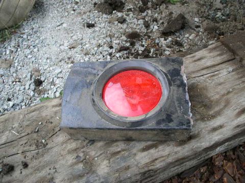 1979 Ford Bronco - A detached taillight assembly with a red lens sits on a piece of wood.