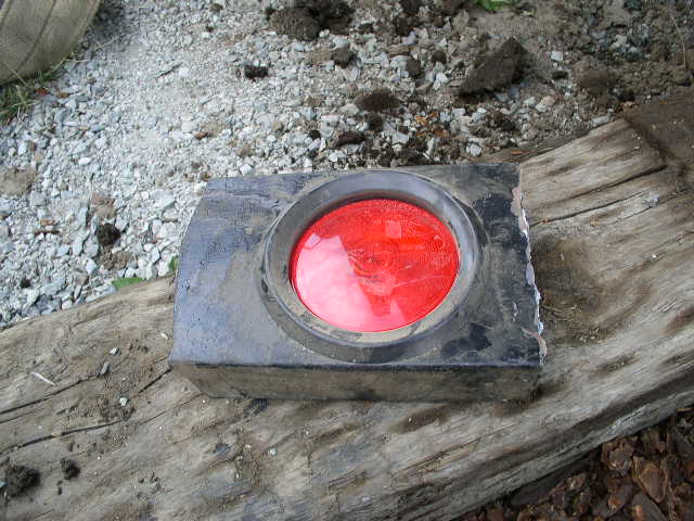 Taillight assembly with red lens, resting on weathered wood