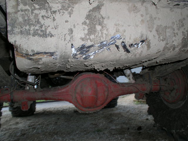 Underside view of a red-painted solid rear axle and differential under a muddy truck