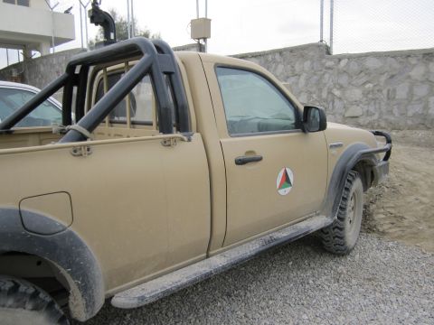 2003 Jeep Wrangler - A tan pickup truck is parked on a gravel surface next to a stone wall.