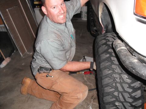 1991 Ford Bronco - A mechanic is shown working on the suspension of a vehicle with large off-road tires.