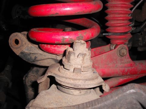 1991 Ford Bronco - Close-up view of vehicle suspension parts, including a red coil spring and shock absorber.