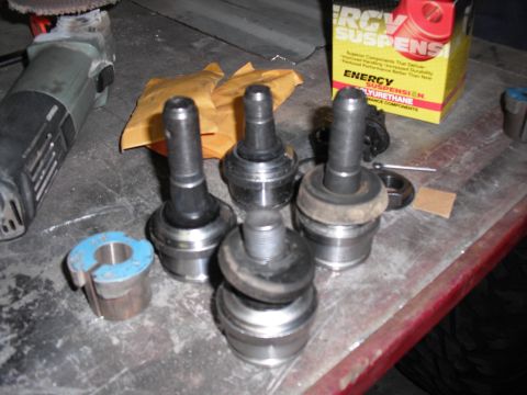 1991 Ford Bronco - Various ball joints and suspension components are laid out on a workbench next to a grinder and a box of Energy Suspension parts.