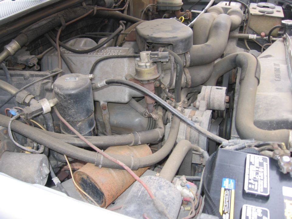 Dusty engine bay showing air pump, hoses and battery in an older vehicle