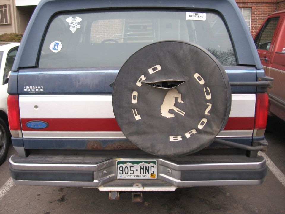 Blue Ford Bronco with red and white stripe, spare tire cover with horse logo, Colorado license plate