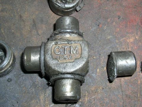 1979 Ford Bronco - A CTM USA universal joint part, likely from a vehicle, lies on a dirty workbench next to other disassembled components.