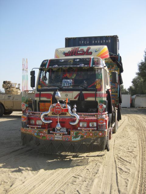 2003 Jeep Wrangler - A brightly decorated truck with intricate patterns and Arabic script is parked on a sandy road, with a military vehicle visible in the back…
