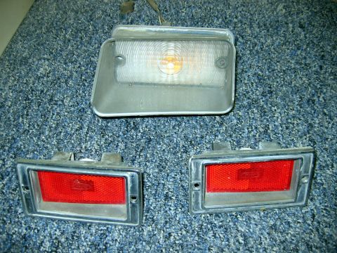 1971 Ford Ranchero - A collection of vehicle lights, including a clear front marker light and two red rear marker lights, are displayed on a textured surface.