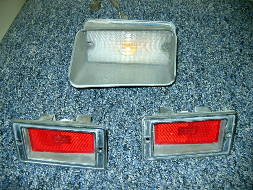 Three vehicle lights on a carpeted surface. One clear lens with a bulb, and two red lenses