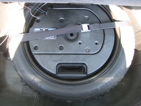 1993 Ford Probe - Spare tire and Bose subwoofer assembly located in the trunk of a vehicle, held in place by a strap.