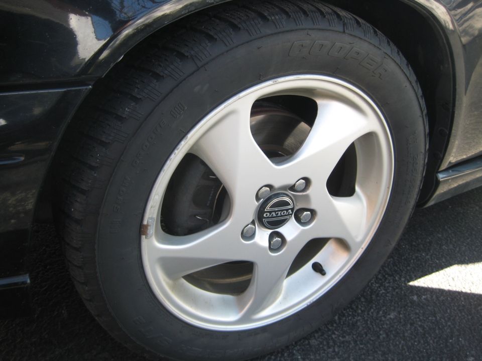 Silver five-spoke wheel with a Volvo logo on a black car