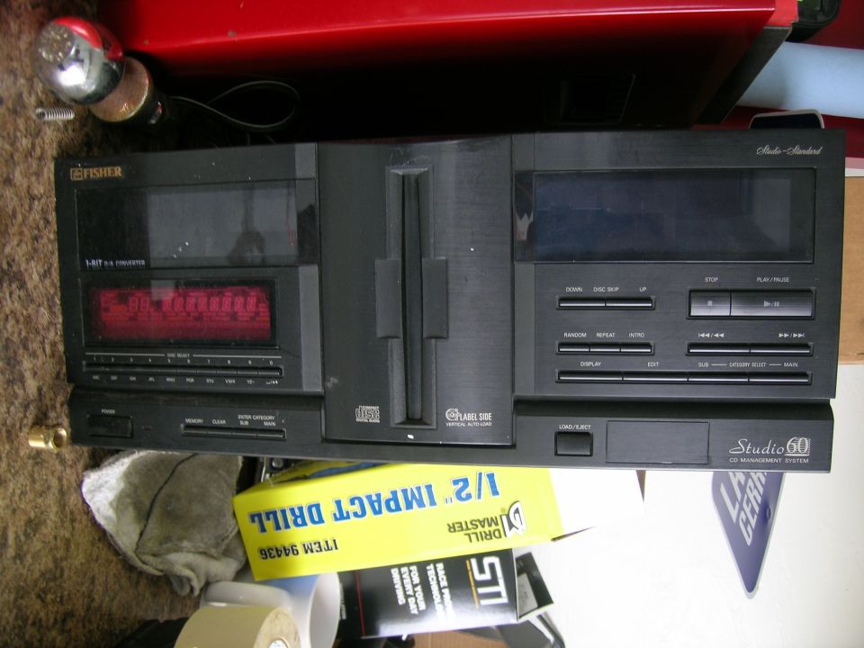 Black Fisher Studio 60 CD changer with red display, photographed sideways among garage clutter