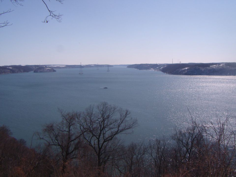 Waterway with sailboats and a small boat, distant bridges, and snow-dusted shores