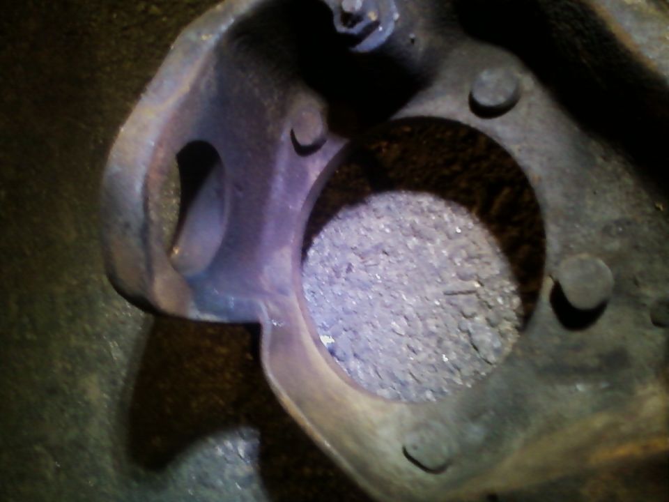 Close-up of a rusty, metallic axle housing part with a circular opening filled with debris