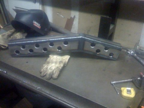 1994 Jeep YJ - A metal part with multiple holes sits on a workbench next to a welding helmet and gloves.