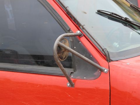1986 Ford Bronco - Close-up of a red SUV's side door and window, showing a custom roll cage mirror mount.