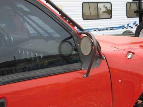 1986 Ford Bronco - Close-up of a red off-road vehicle's side, a roll cage and a large, utilitarian side mirror.