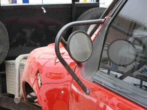 1986 Ford Bronco - Close-up of a red 1986 Ford Bronco fender and side mirror with a custom roll cage.