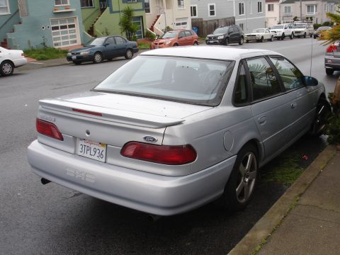 1989 Ford Taurus - A silver sedan is parked on a residential street, showing its rear end and license plate.