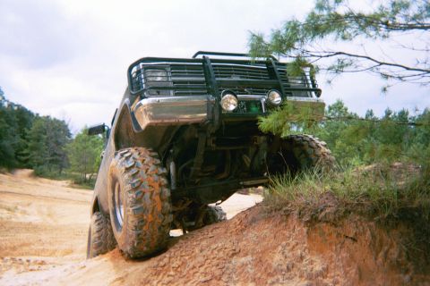 1985 Ford Bronco - This SUV is tackling a steep dirt incline, its large tires gripping the loose soil.