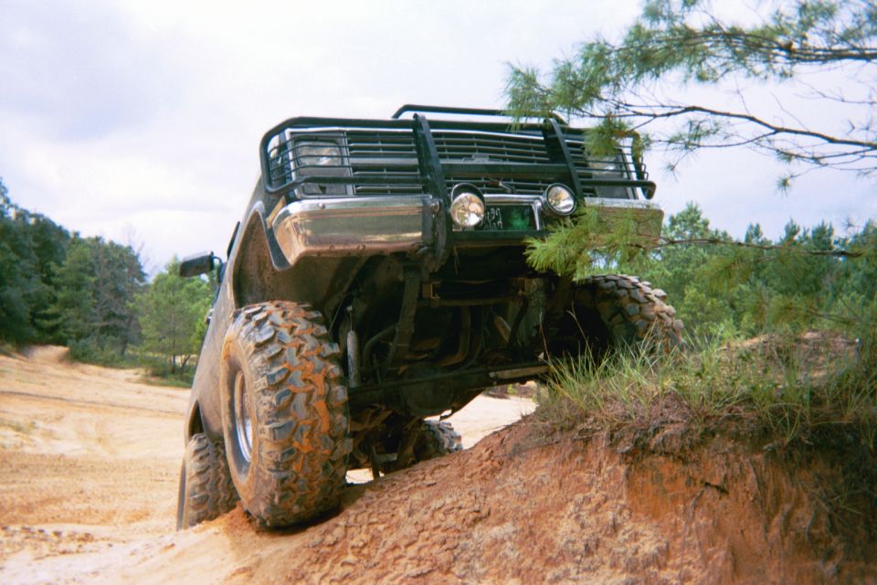 Off-road SUV with large tires climbing a dirt hill, front bull bar visible