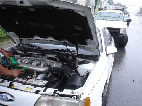 1989 Ford Taurus - Someone is performing maintenance on the engine of a white Ford Taurus SHO on a rainy day.