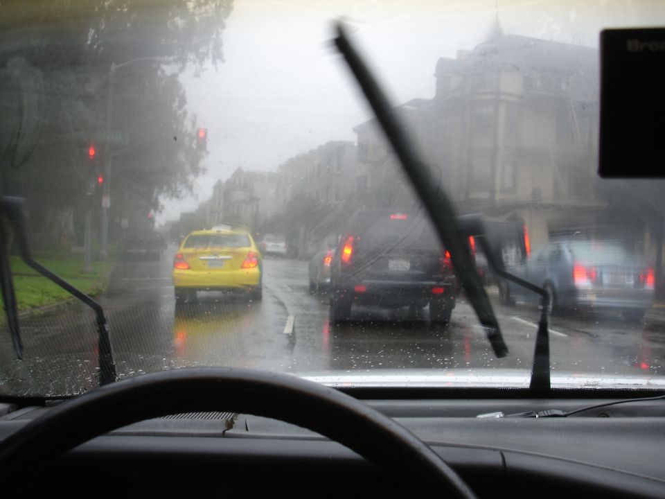 View from inside a vehicle looking out the windshield on a rainy day, with traffic ahead