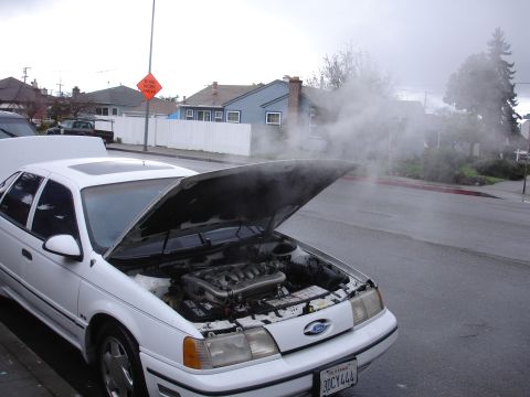 1989 Ford Taurus - White 1989 Ford Taurus overheating on a residential street, steam escaping from the engine.