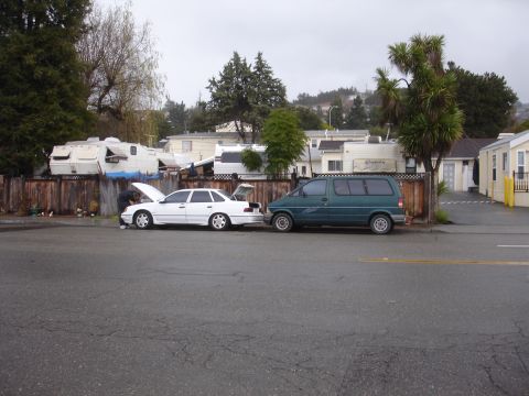 1989 Ford Taurus - Two vehicles are parked on a street, one with its hood and trunk open, suggesting maintenance.