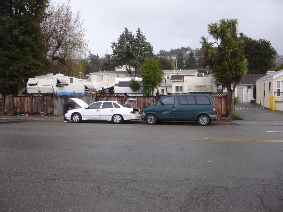 1989 Ford Taurus sedan with hood and trunk open, parked next to a green van